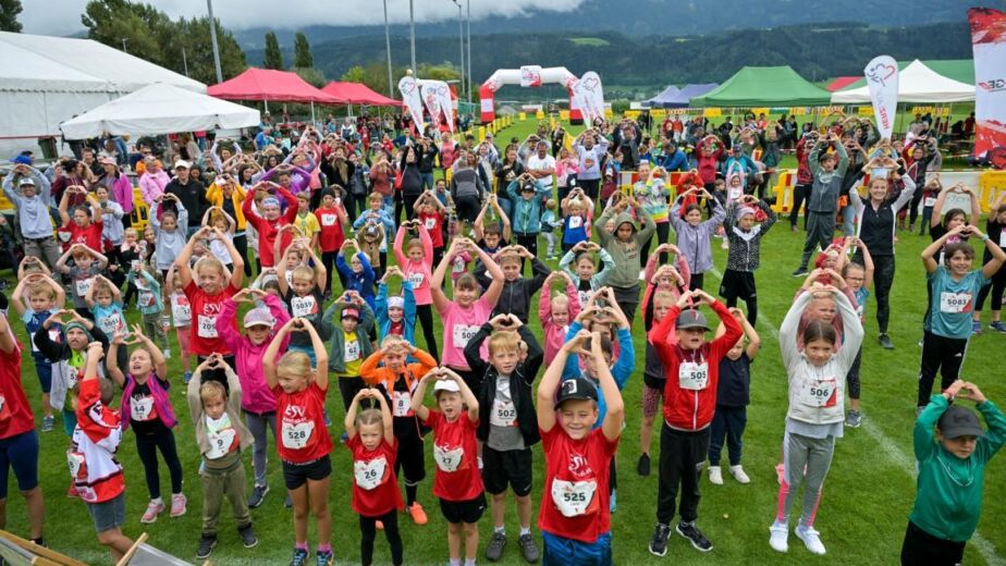 Eine Gruppe von Menschen (größtenteils Kinder) steht auf einem Sportplatz und formt mit den Händen ein Herz © C&D Moser, Foto Moser